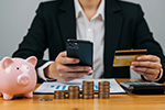 Mann mit Smartphone, Bankomatkarte, Sparschwein und Münzen